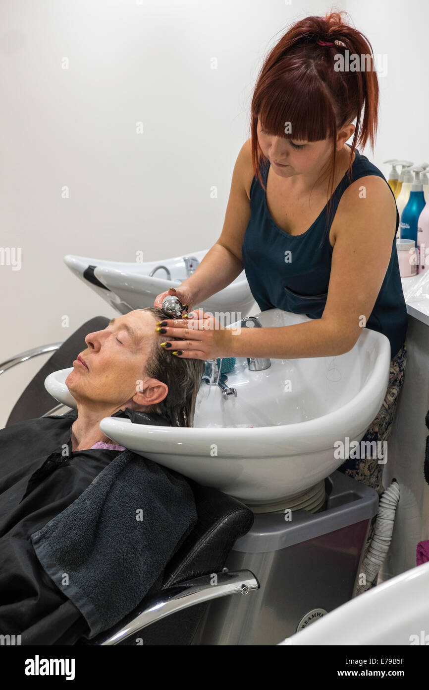 ÄLTERE FRAU IM FRISEURSALON DIE HAARE GEWASCHEN VON JUNGER AUSZUBILDENDER FRISEUR ENGLAND UK Stockfoto
