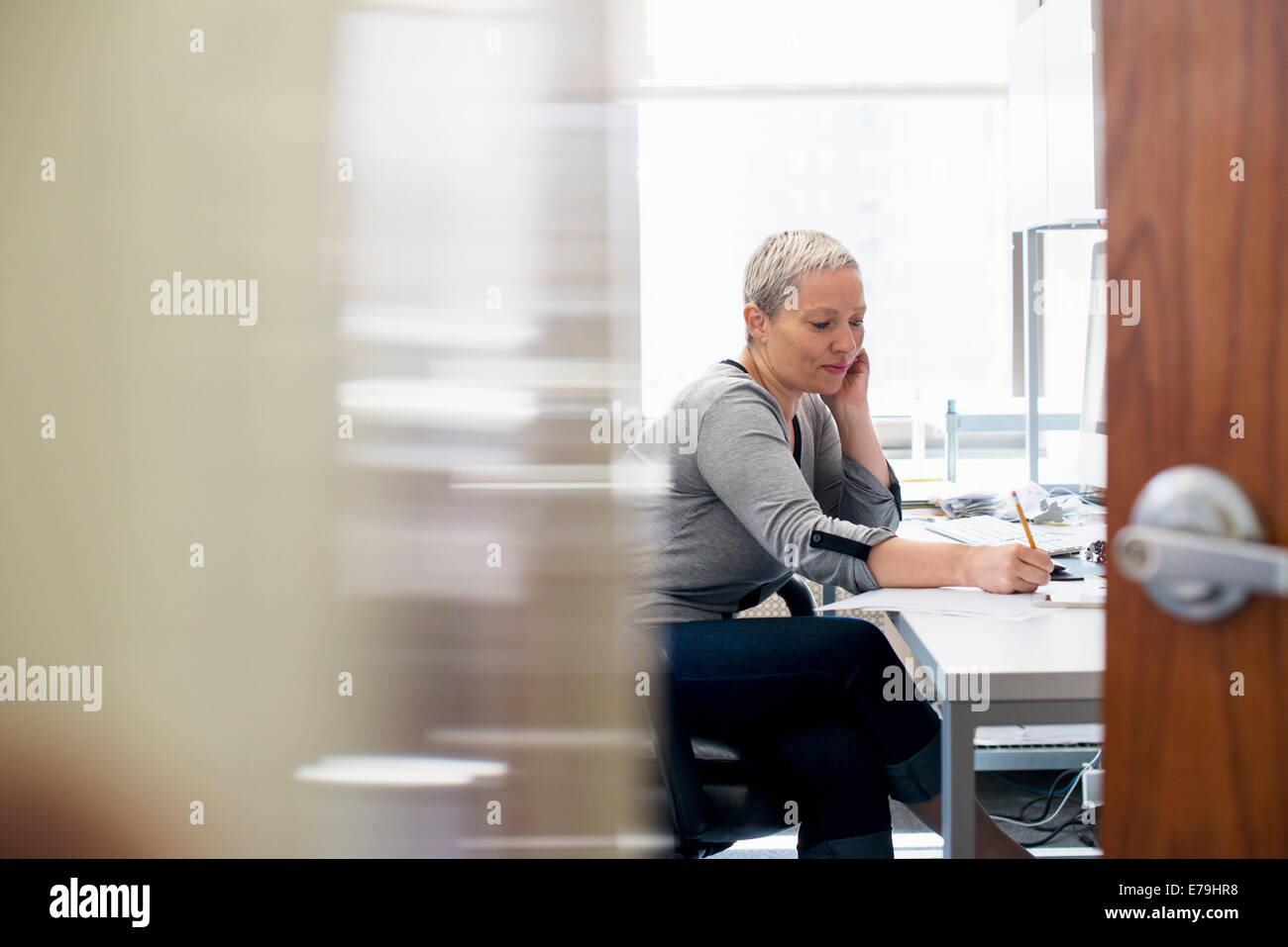 Eine Frau arbeitet in einem Büro alleine. Konzentration auf eine Aufgabe, die Notizen mit einem Bleistift. Stockfoto