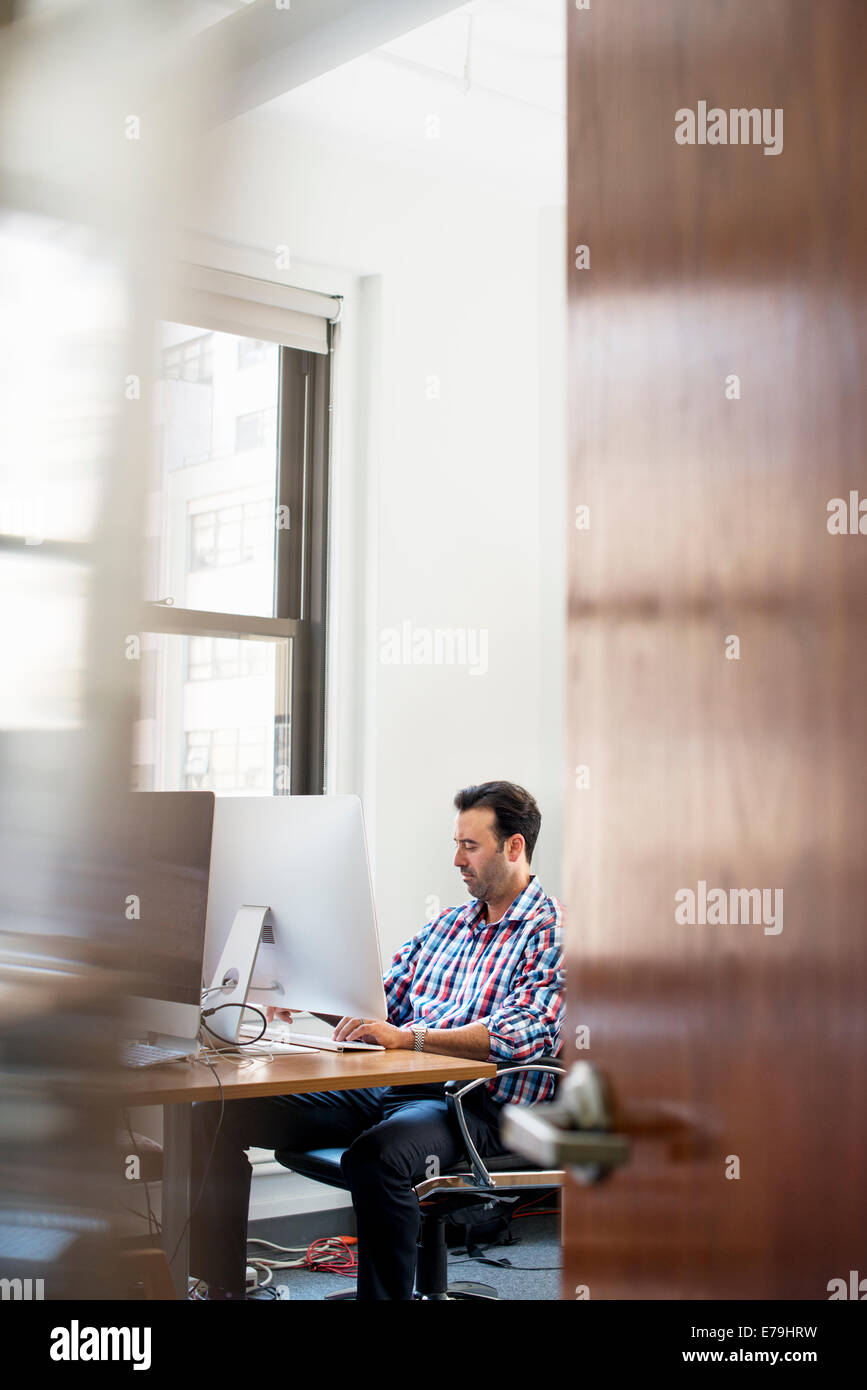 Ein Mann in einem Büro an einem Schreibtisch mit einem Computer arbeiten. Stockfoto