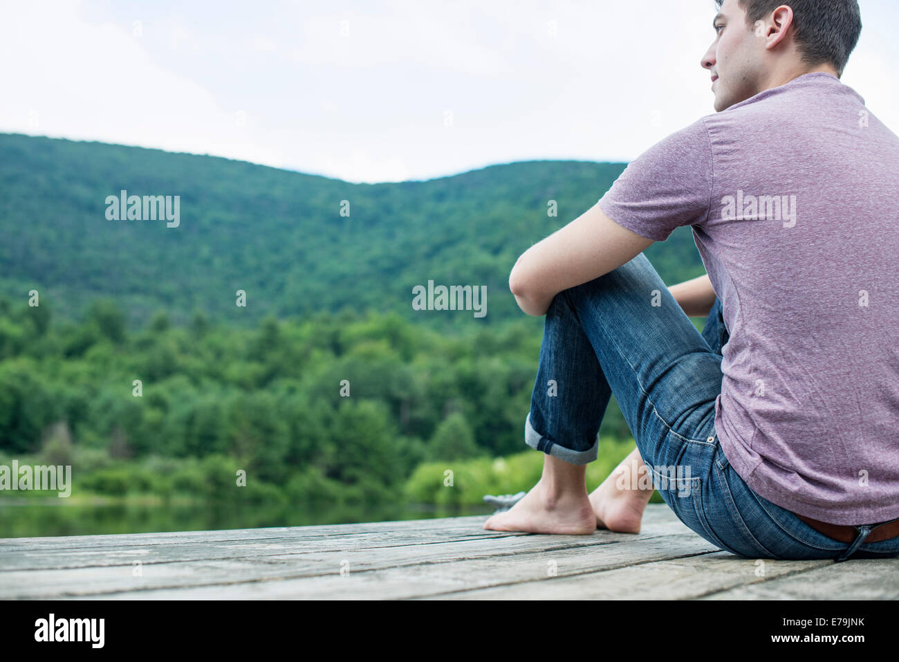 Ein Mann sitzt auf einem hölzernen Pier an einem See im Sommer Stockfoto