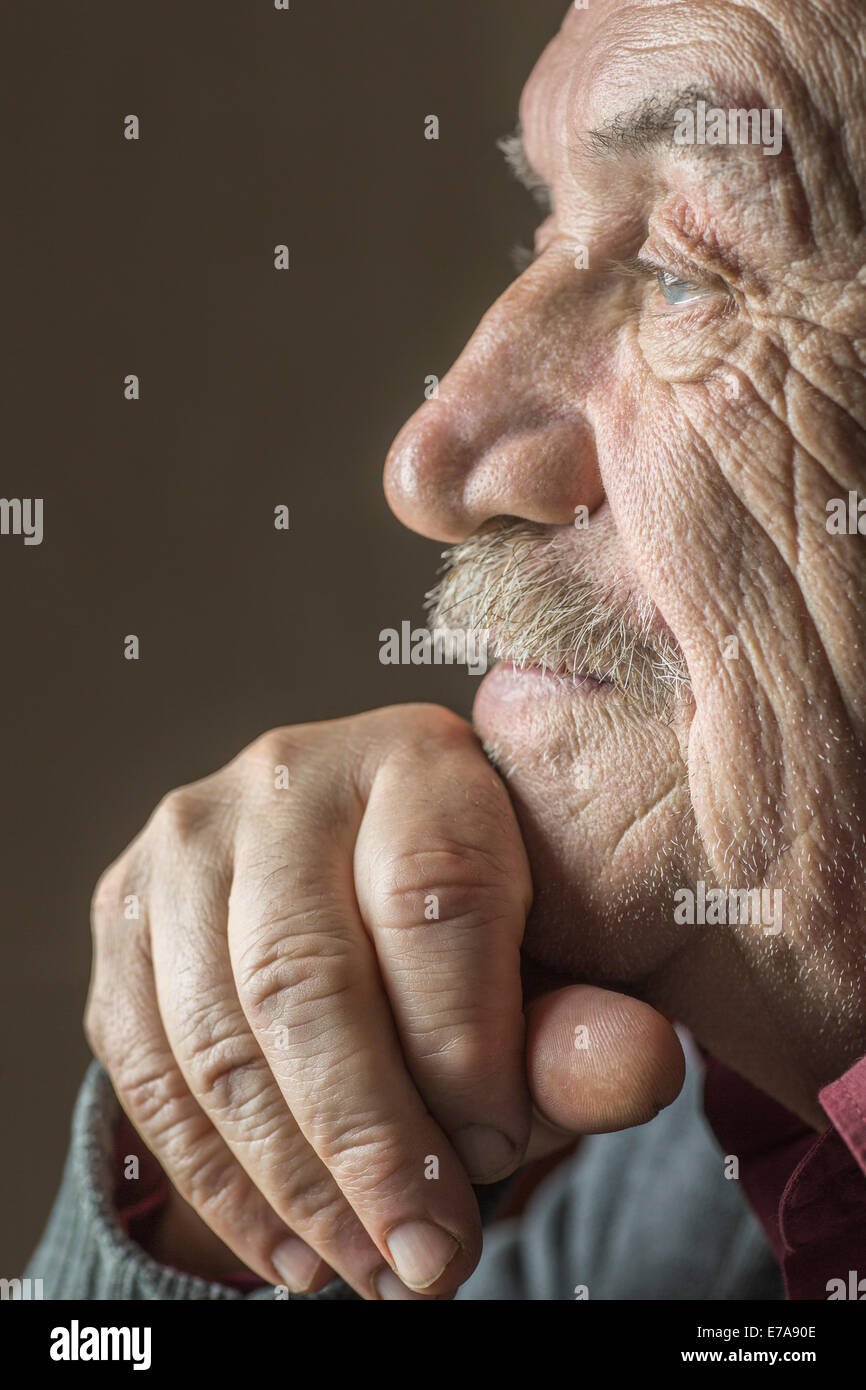 Nahaufnahme Seitenansicht des nachdenklichen älteren Mann mit Hand am Kinn auf braunem Hintergrund Stockfoto