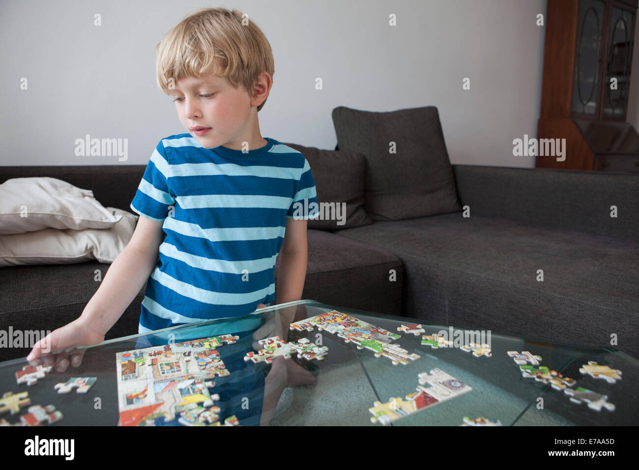 Junge Lösung Puzzle auf Glastisch im Wohnzimmer zu Hause Stockfoto