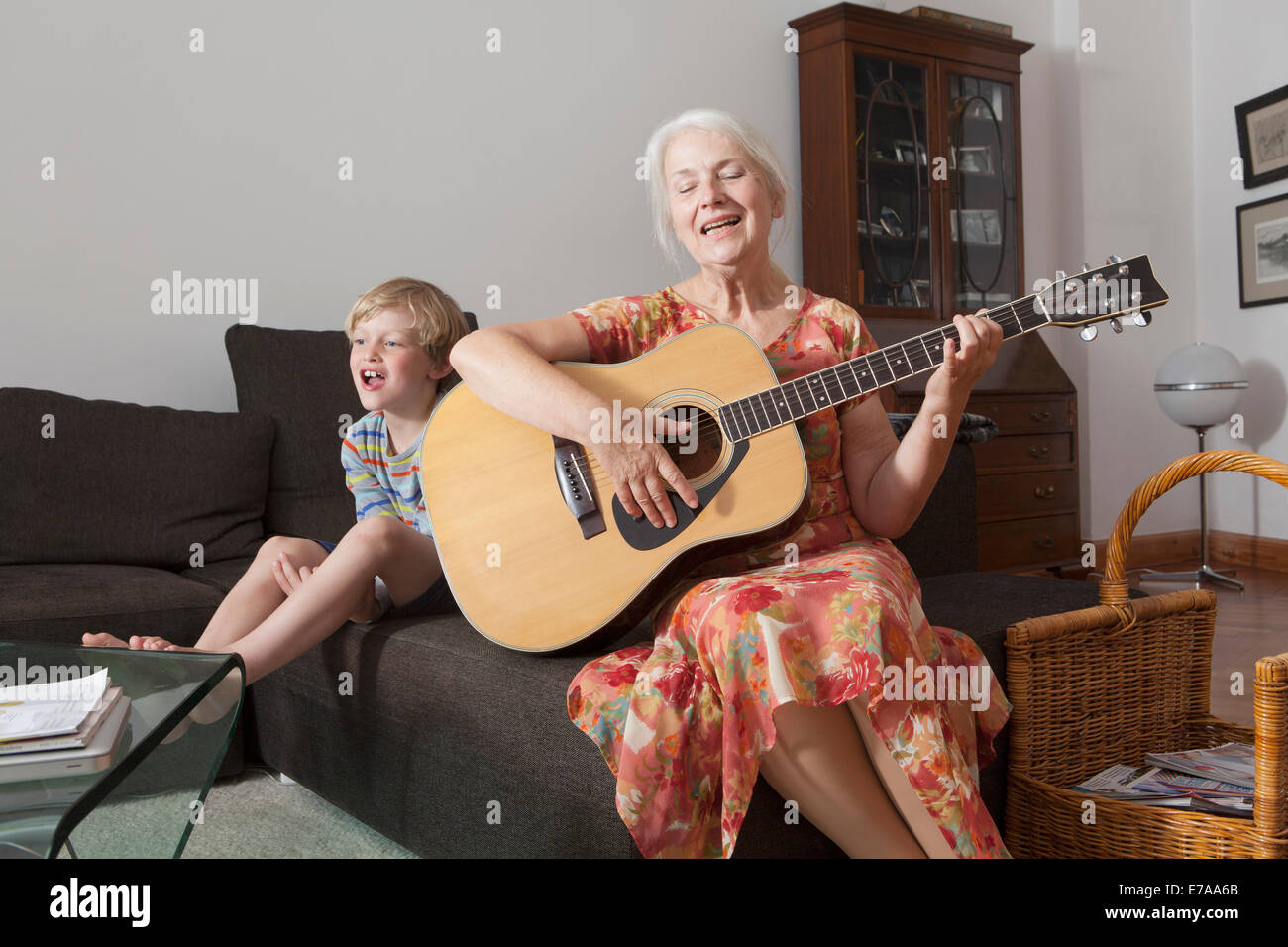 Verspielte Junge sitzt mit Großmutter singen und Gitarre zu spielen, zu Hause auf sofa Stockfoto