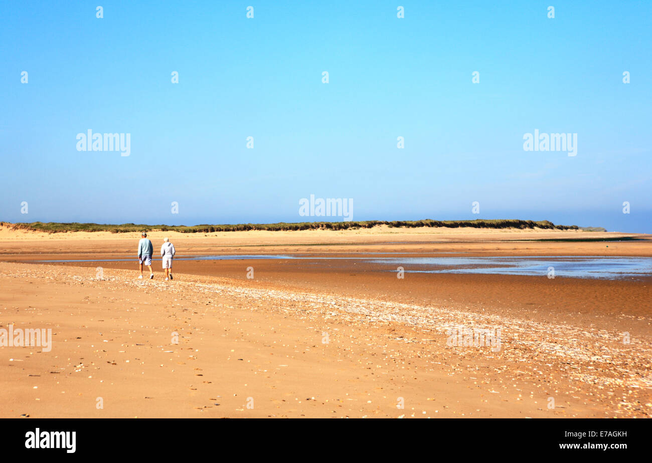 Ein älteres Ehepaar zu Fuß auf einem breiten Sandstrand in North Norfolk am Burnham Overy, Norfolk, England, Vereinigtes Königreich. Stockfoto