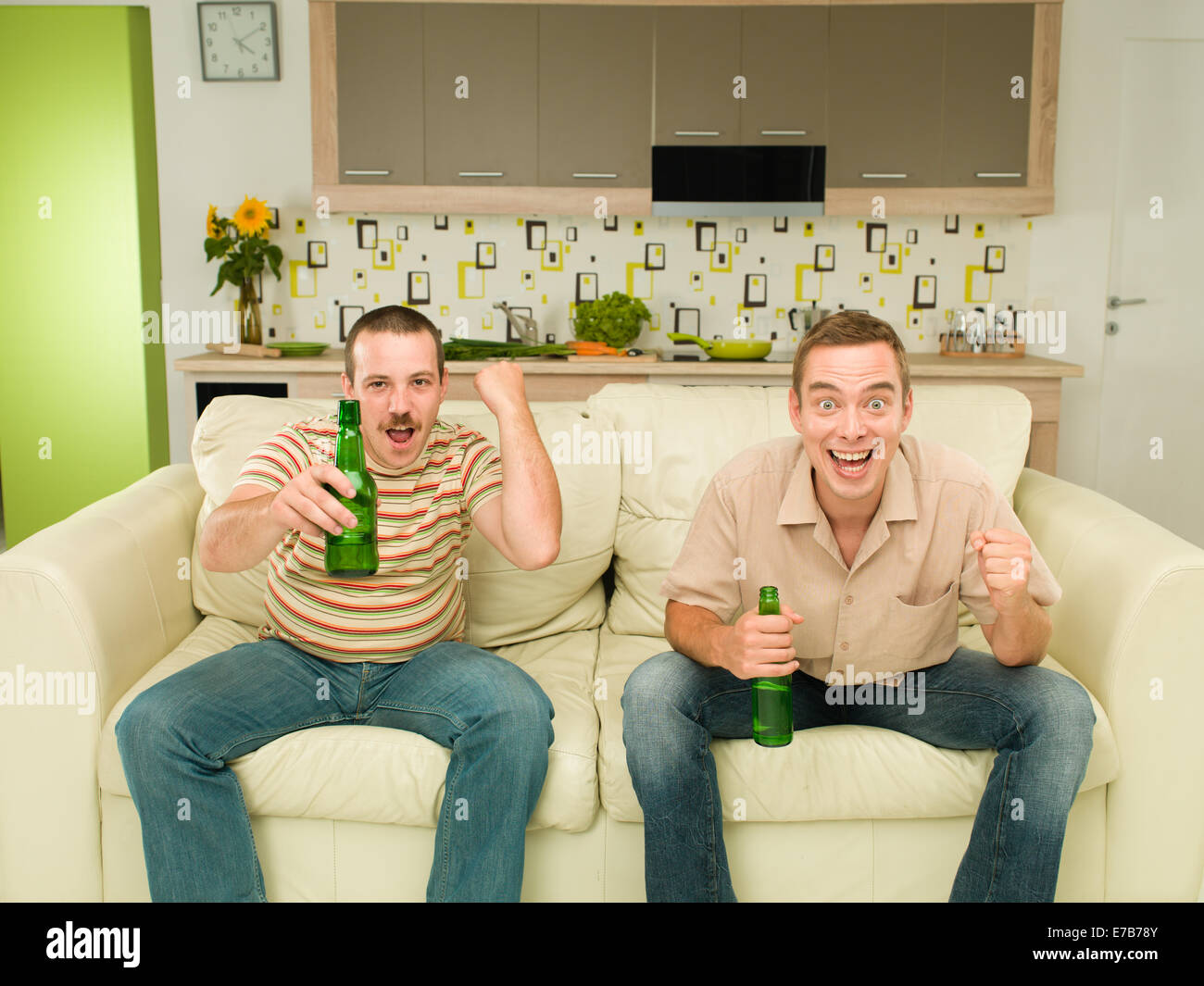 zwei Männer sitzen auf der Couch vor dem Fernseher, in Küche, halten Bären und schreien aufgeregt Stockfoto