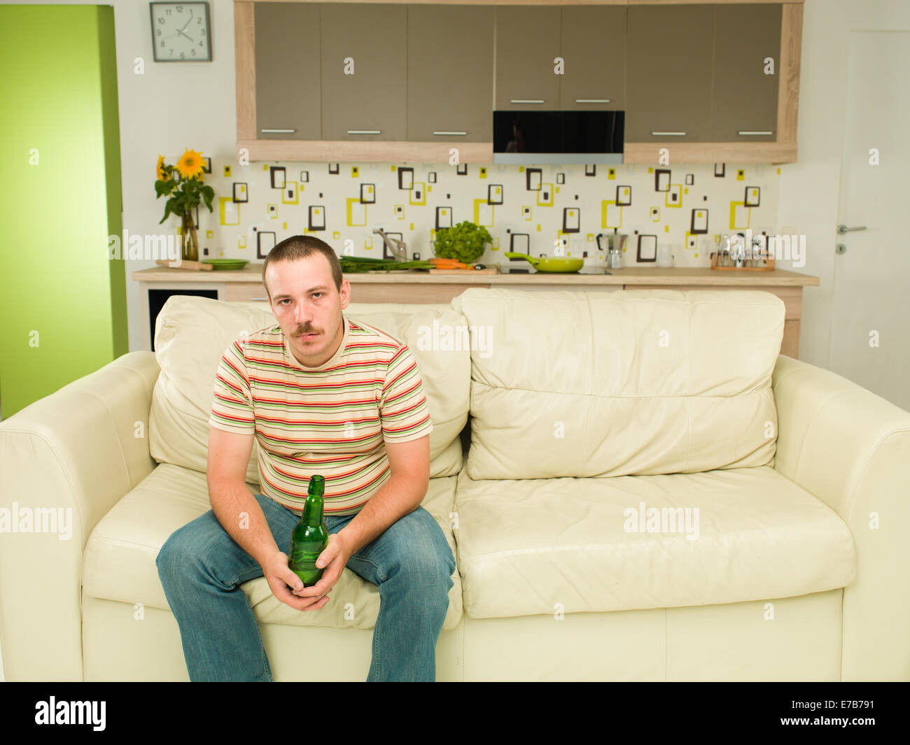 Vorderansicht des kaukasischen Mann sitzt auf der Couch, die Bierflasche in seinen Händen hält, müde suchen Stockfoto