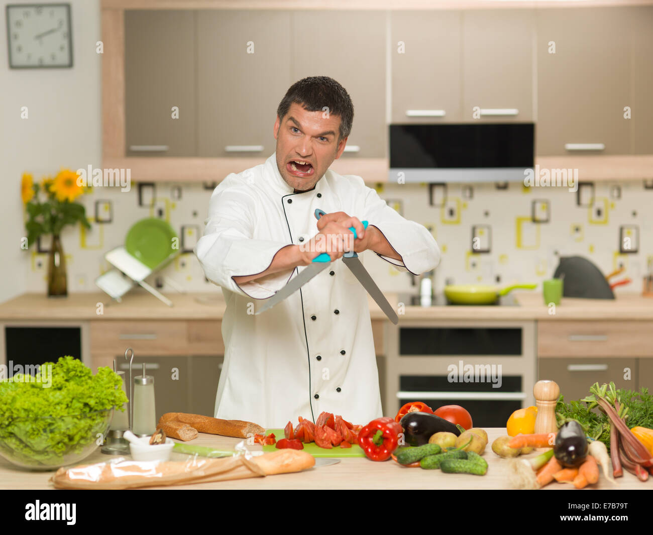 wütend Koch vor Tisch mit Gemüse, mit zwei Messern Stockfoto