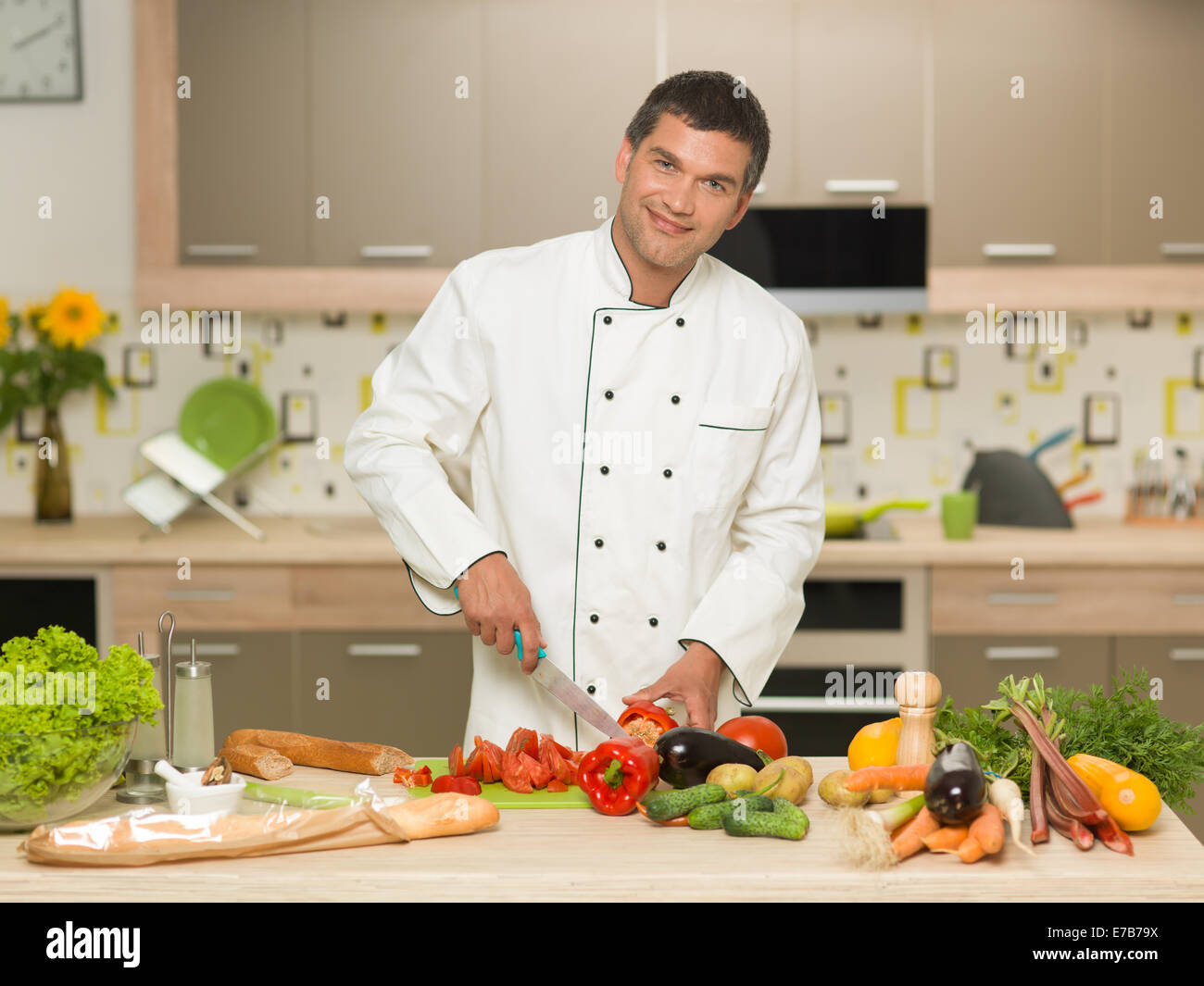 Frontansicht des kaukasischen Mann mit Koch Kleidung, Schneiden von Gemüse in der Küche, Lächeln Stockfoto