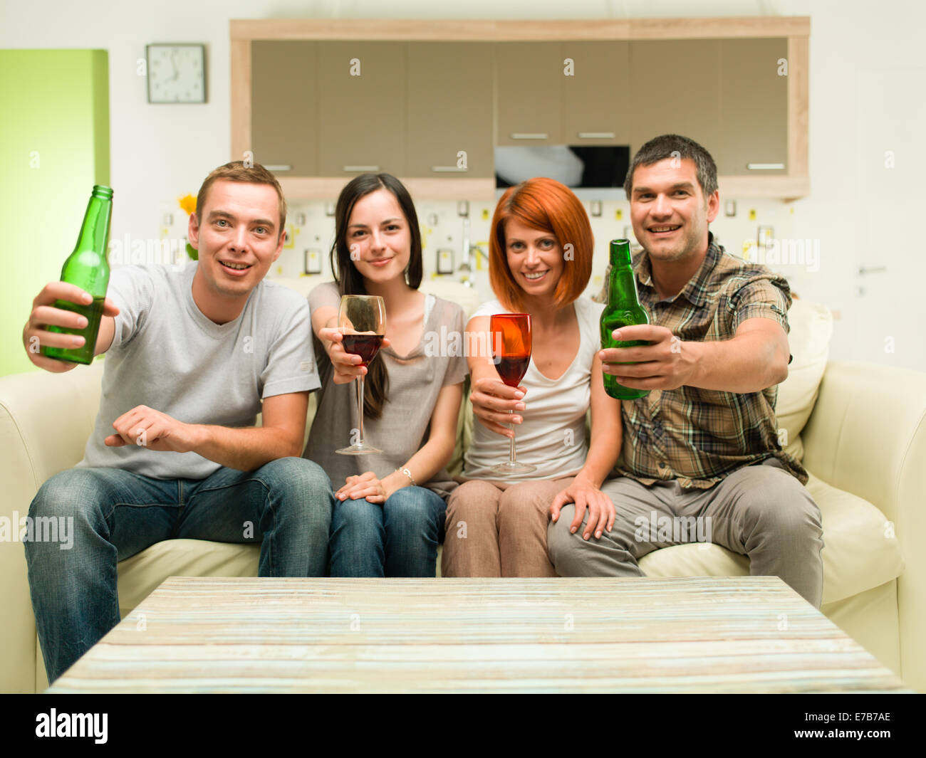 Freunde zu Hause auf dem Sofa sitzen, machen einen Toast mit Getränken und vor dem Fernseher Stockfoto