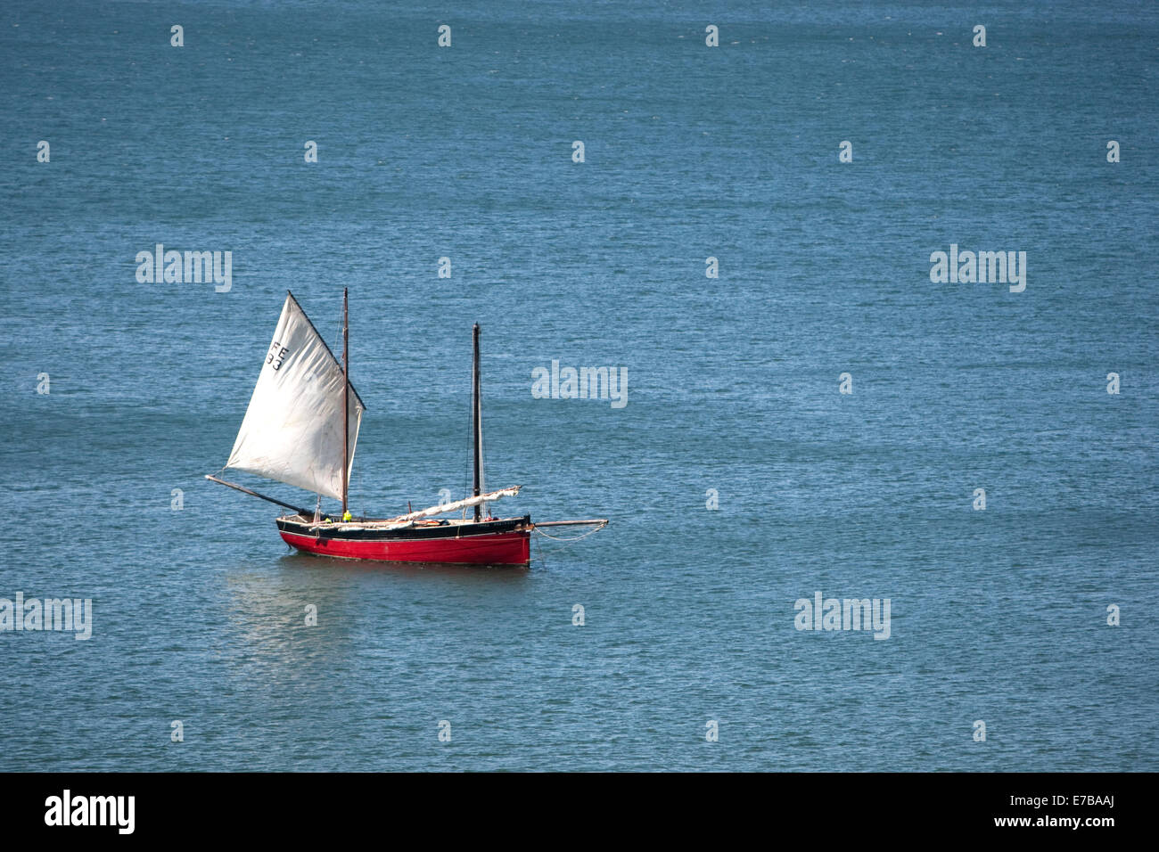 Ein kleines rotes Boot mit einem weißen Segel am blauen Meer Stockfoto