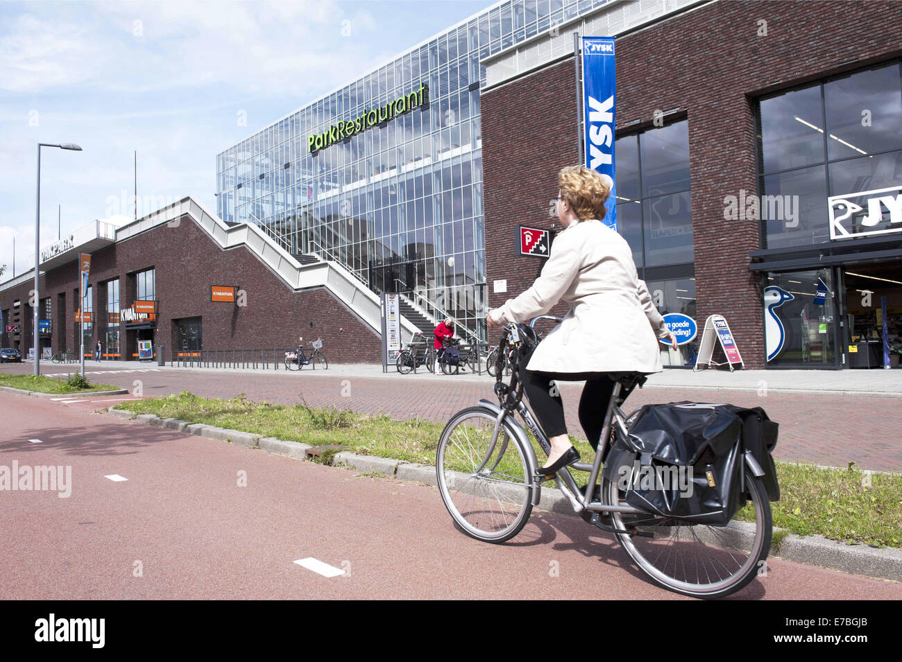 Rotterdam, Zuid-Holland, Niederlande, Holland. 29. August 2014. Eine Frau Zyklen entlang eines Shopping Centers. Am Anfang dieses Einkaufszentrum ist ein großer Park. In Rotterdam ist der größte öffentliche Park auf eines Geschäftshauses in Europa. Auf 9 Meter hoch, am oberen Bigshops Marconi Plaza ist ein grüner Park mit drei Themengärten. Der Park misst acht Hektar und bietet einen Blick auf die Stadt und den Hafen. Es ist 800 Meter lang, 80 Meter breit und 9 Meter hoch. Unterhalb des Parks ist 25.000 m2 Verkaufsfläche. Es ist nicht nur ein Einkaufszentrum und ein Ort, wo Sie, zur gleichen Zeit neu erstellen können, die es einem da ist Stockfoto