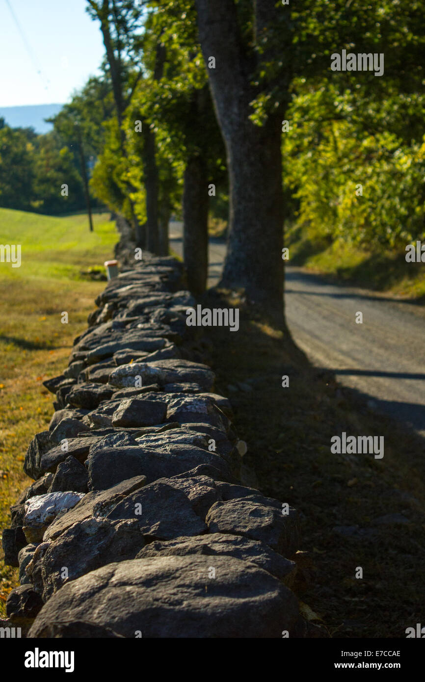 Stein auf dem Bauernhof Wand über eine ländliche Schotterstraße. Stockfoto