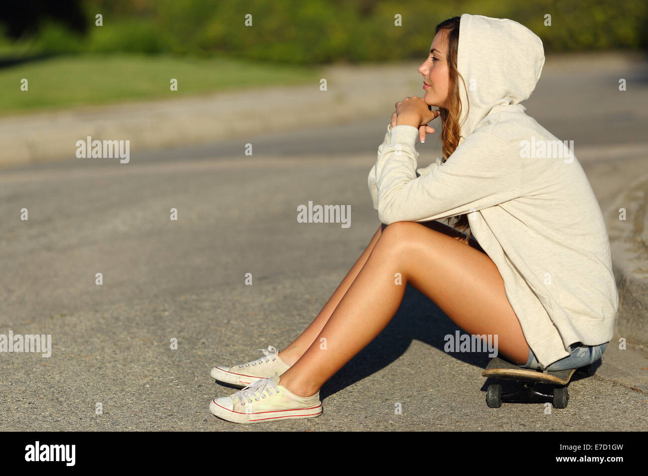 Ganzkörper eines Profils ein nachdenklich Teenager-Mädchen sitzen auf einem Skate auf der Straße, auf der Suche nach Stockfoto