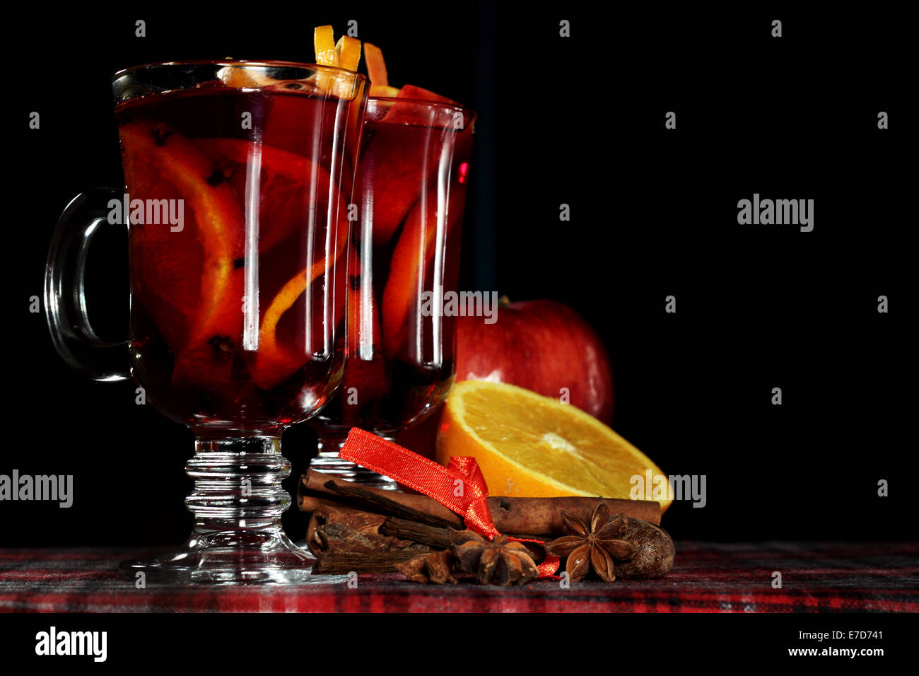 Heiße rote Glühwein mit Früchten und Zimt auf karierten Tischdecke Stockfoto