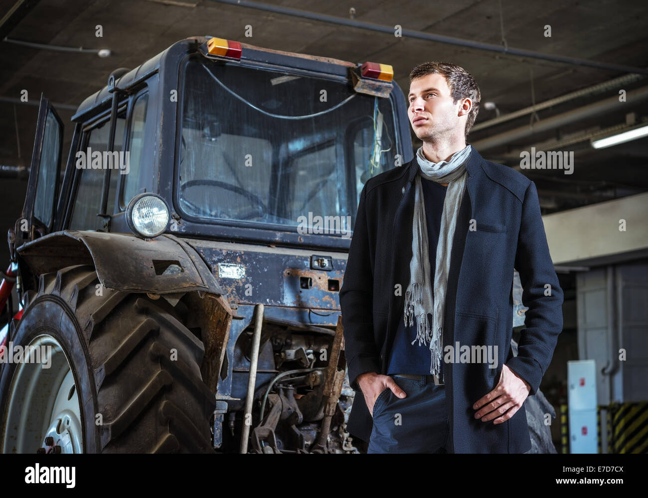 Mode geschossen: ein hübscher junger Mann in Jeans und Mantel gegen den Traktor Stockfoto
