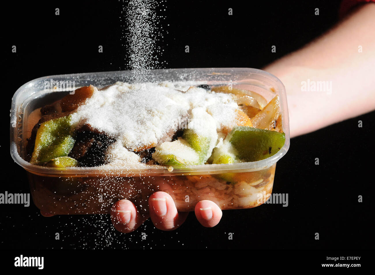 Eine Frau gießt Salz auf eine ungesunde Mahlzeit zum mitnehmen. Stockfoto