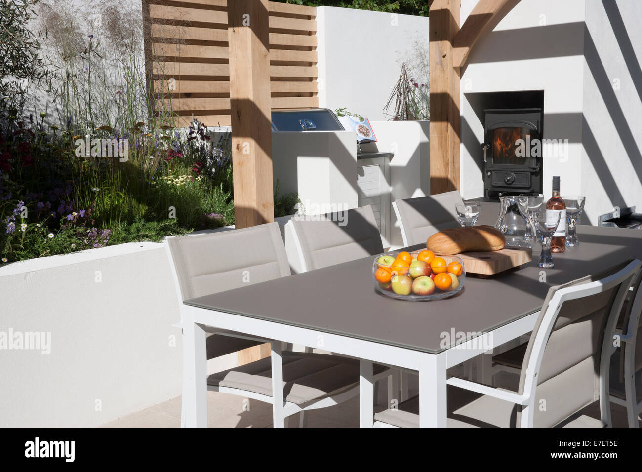 Garten - Al Fresco - Blick auf den modernen Garten Essensmöbel Wohnbereich Terrasse mit Tischen und Stühlen Holzofen im Freien Großbritannien Stockfoto