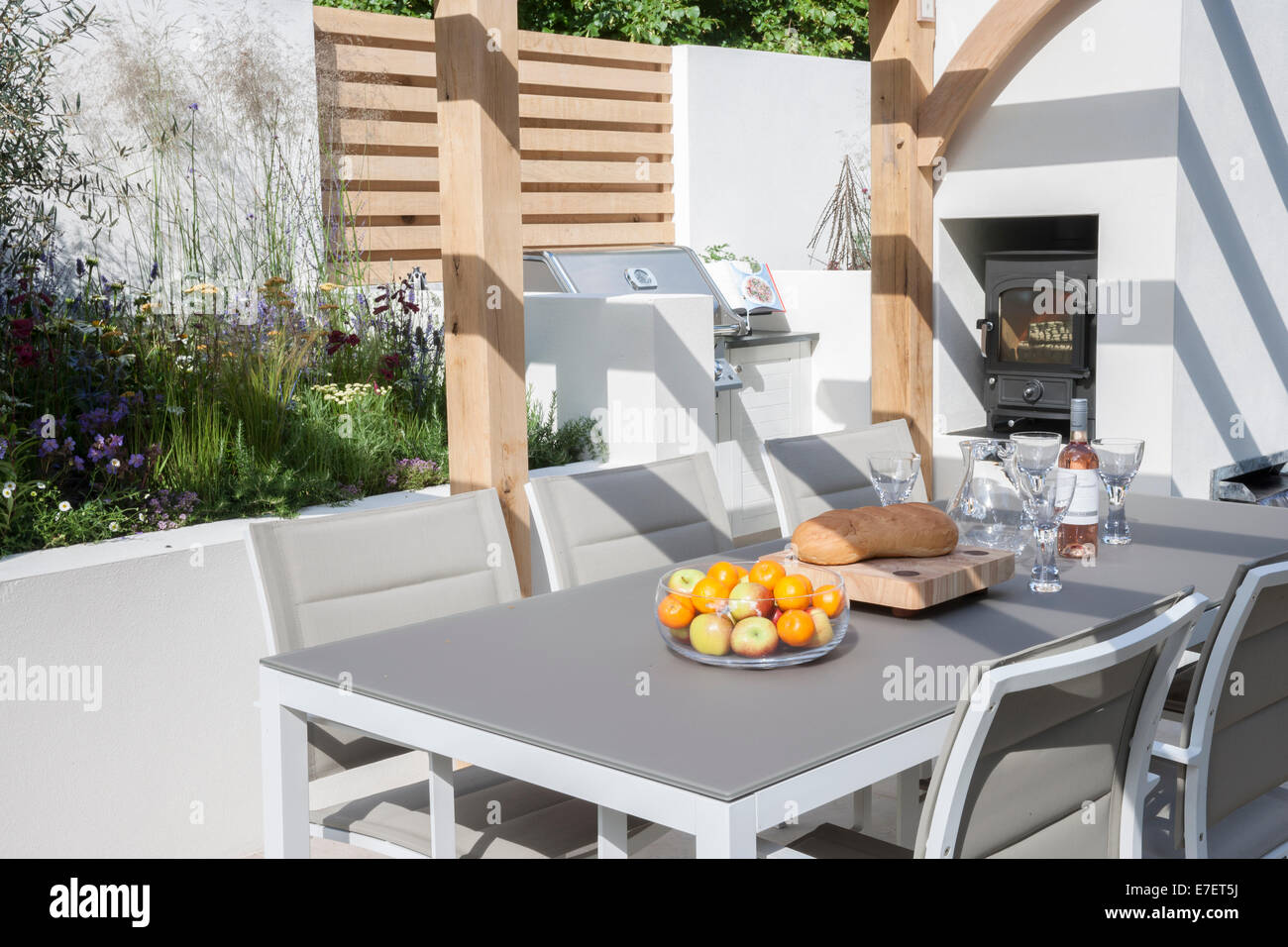 Garten - Al Fresco - Blick auf den modernen Garten Essensmöbel Wohnbereich Terrasse mit Tischen und Stühlen Holzofen im Freien Großbritannien Stockfoto