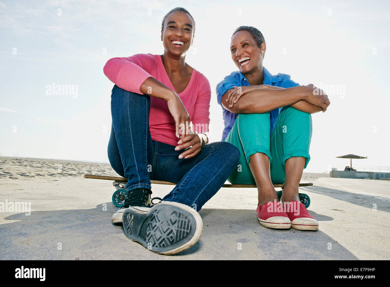 Ältere schwarze Frauen sitzen auf Skateboard am Strand Stockfoto