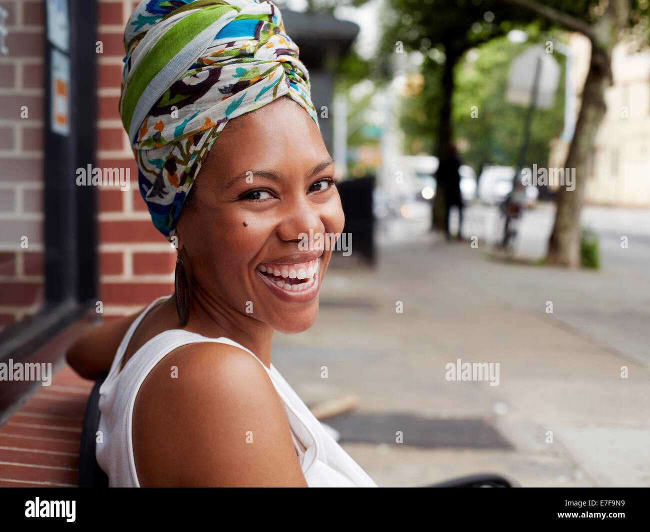 Schwarze Frau lächelnd auf Bank auf Stadtstraße Stockfoto
