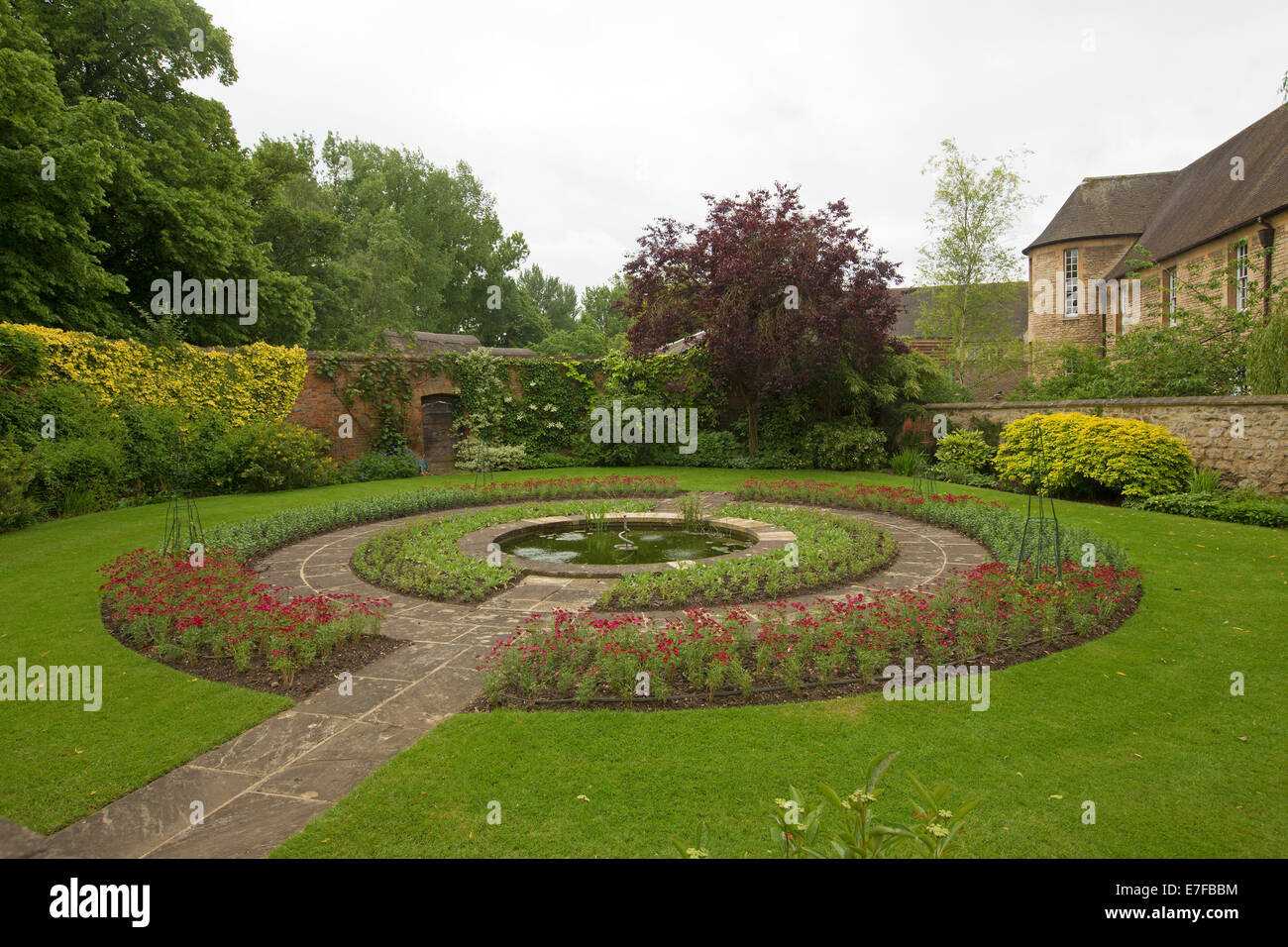 Formale ummauerten Garten mit Weg über smaragdgrünen Rasen führt, Wassereigenschaft, umgeben von großen kreisförmigen Gartenbeete mit roten Blumen runden Stockfoto