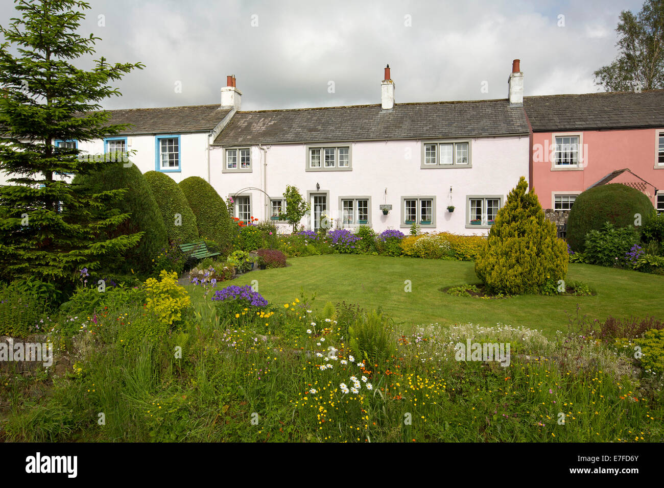 Weiß lackiertes englischen Cottage mit gepflegten Gärten mit Rasenflächen und Massen von bunten Frühlingsblumen und Sträucher im Dorf Caldbeck in Cumbria Stockfoto