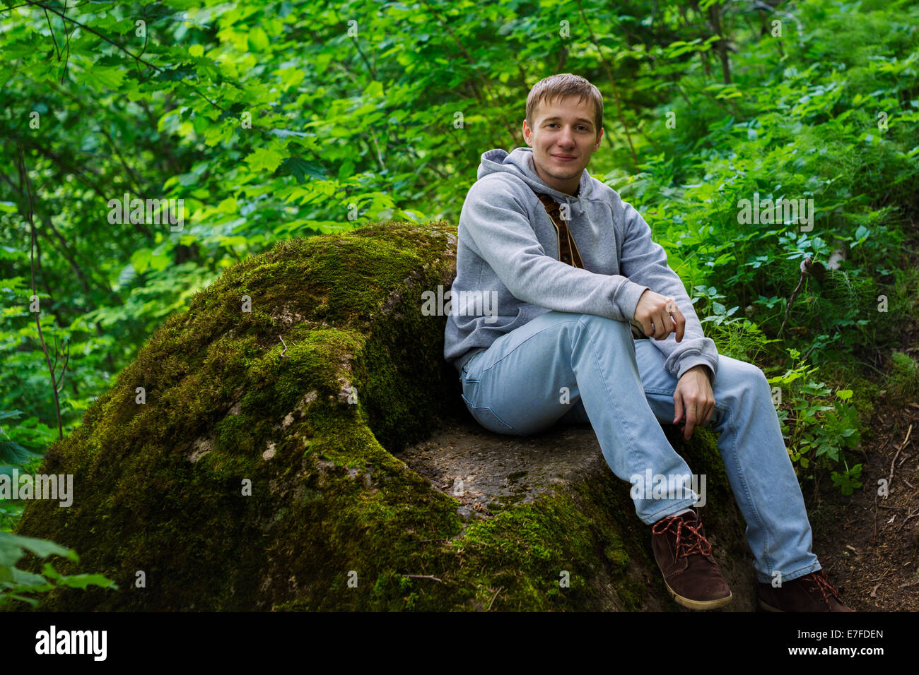 Gut aussehender Mann sitzt auf einem Felsen Stockfoto