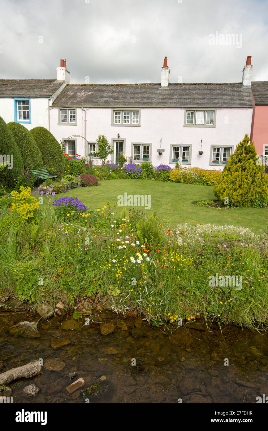 Weiß lackiertes englischen Cottage mit gepflegten Garten, Rasen, Massen von bunten Frühlingsblumen und kleinen Bach im Dorf Caldbeck in Cumbria Stockfoto
