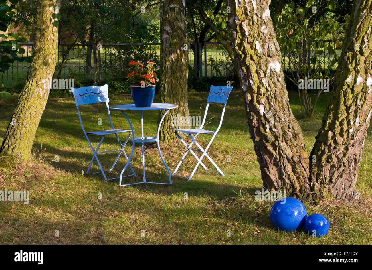 Blauer Tisch, Stühle & Dekoration im Garten mit Bäumen, Stockfoto