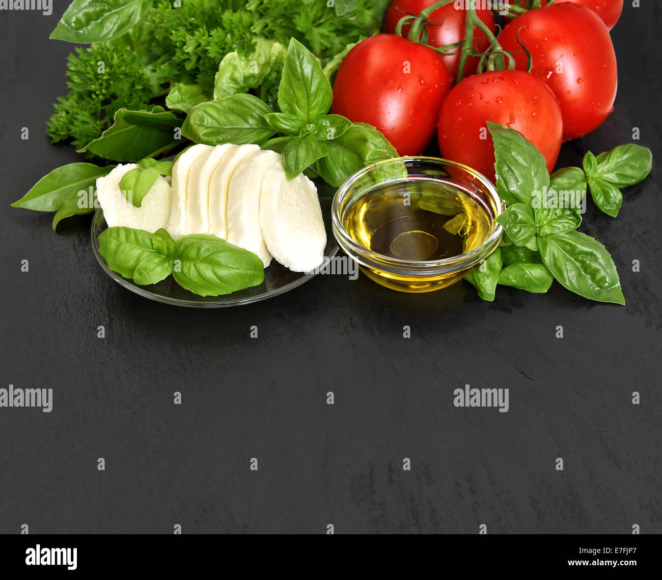 frischem Basilikum, Tomaten, Mozzarella und Olivenöl auf schwarzem Hintergrund. Caprese Salatzutaten Stockfoto