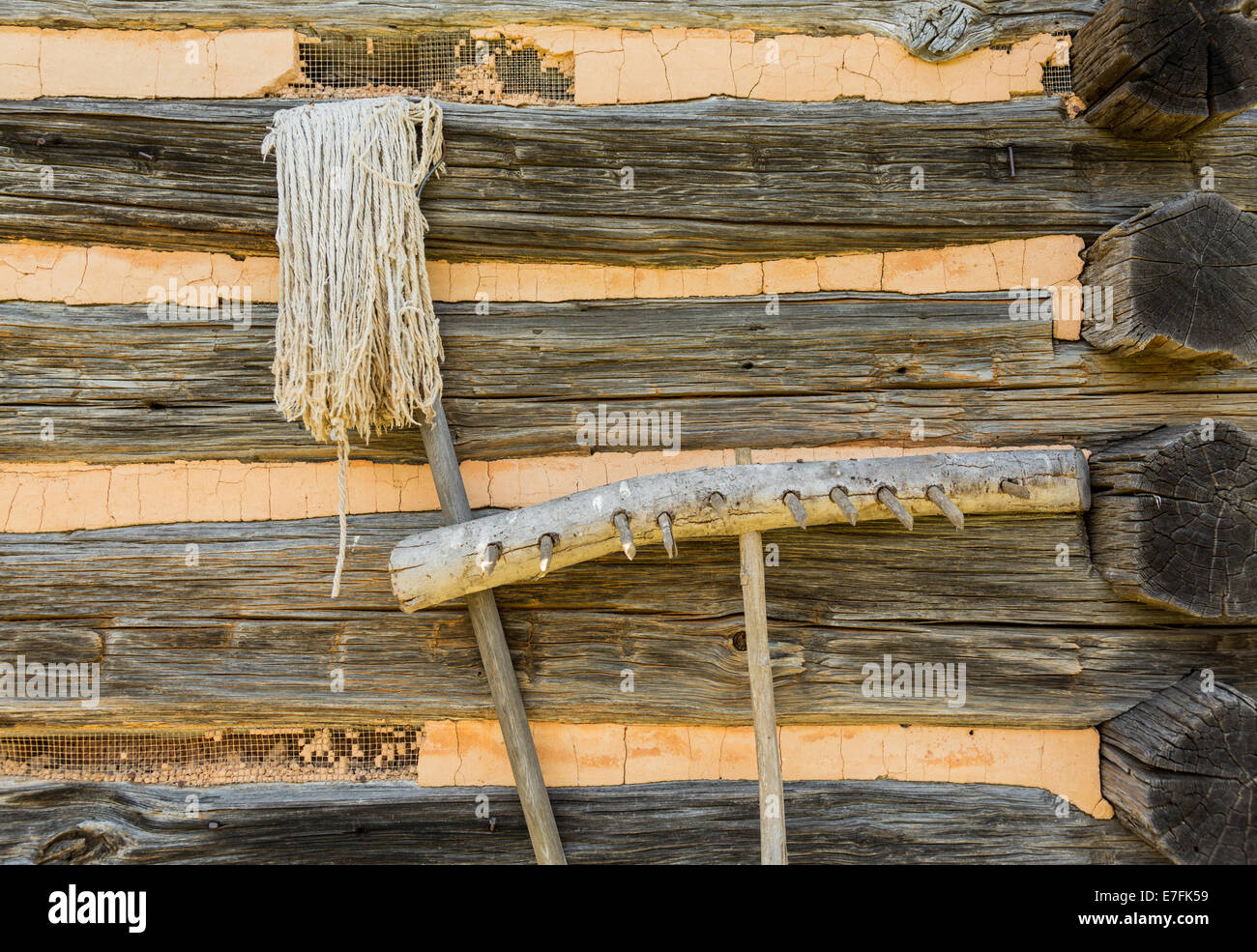 Alte handgemachte landwirtschaftlichen Geräten der hölzernen Rechen und Zeichenfolge Mop Blockhütte Wände gelehnt Stockfoto