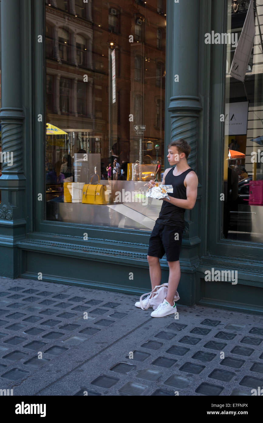 Junge modische Mann Essen ein Mittagessen zum Mitnehmen am Lower Broadway in New York City Stockfoto