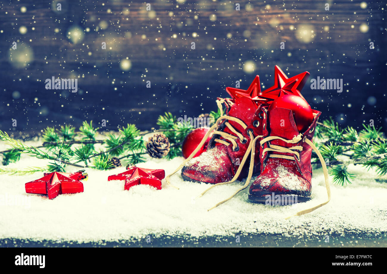 Vintage Weihnachten Dekoration rote Kugeln, Sterne und Antik baby-Schuhe auf hölzernen Hintergrund mit Schneeflocken. Retro-Stil getönten pic Stockfoto