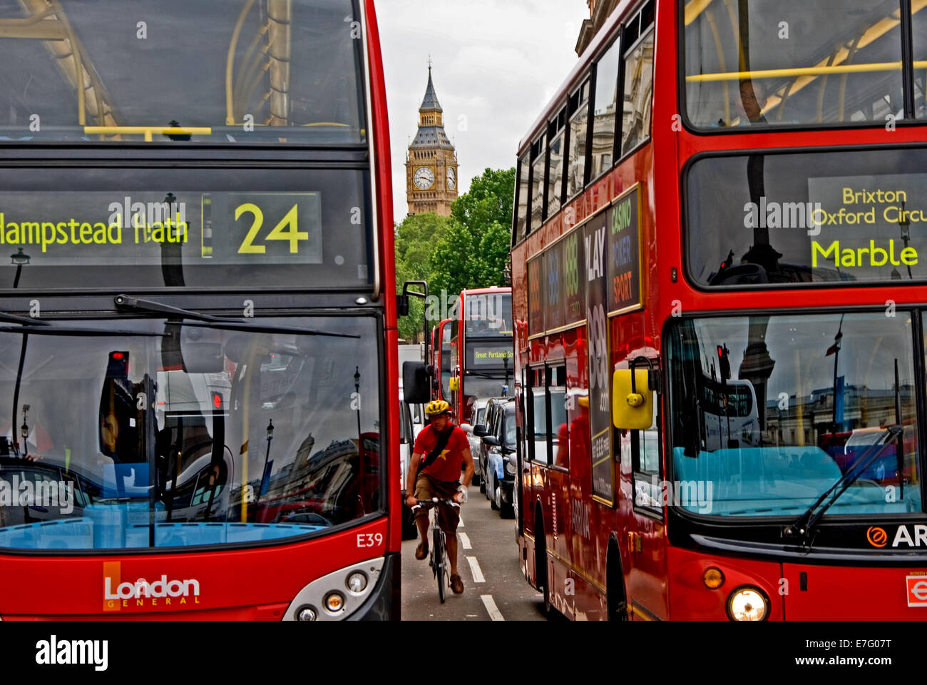 Ein Radfahrer drückt durch einen Spalt zwischen zwei roten Londoner Busse während Sie an der Ampel warten. Stockfoto