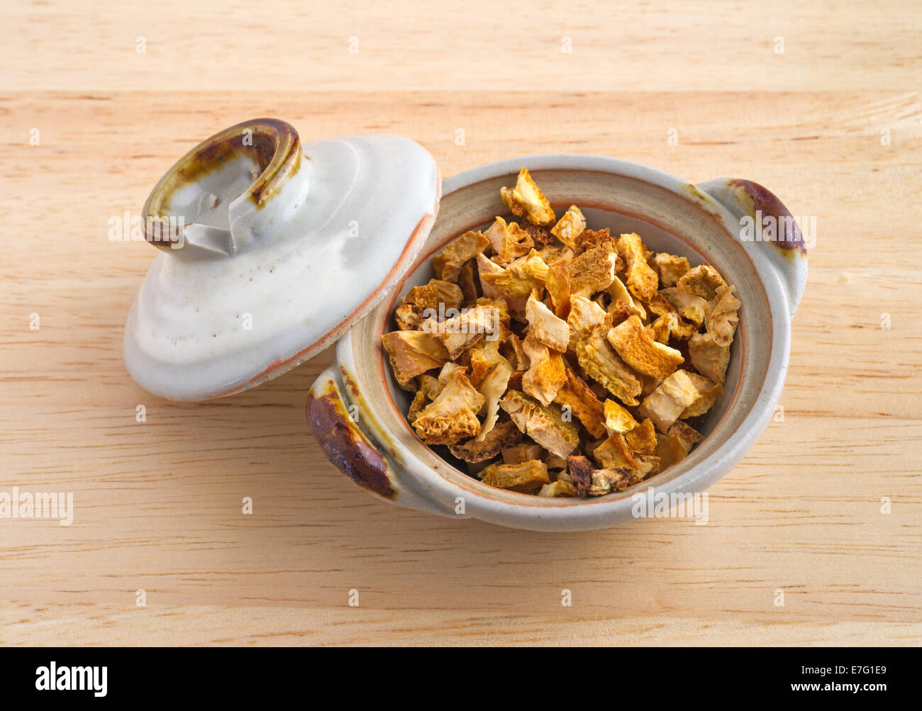 Eine kleine Schale mit separaten Deckel gefüllt mit Stücken von getrockneten Orangenschalen auf einem Holztisch. Stockfoto