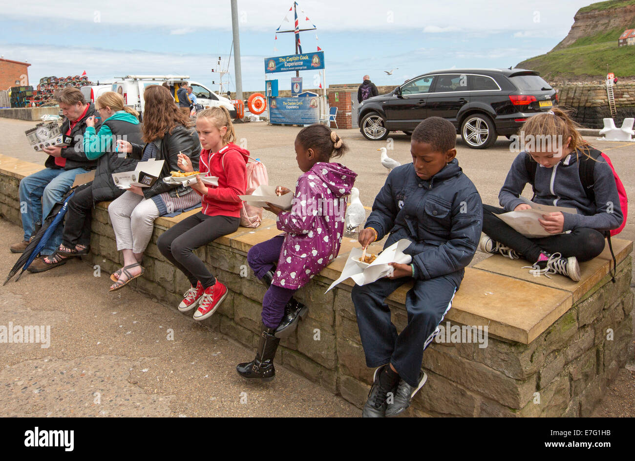 Gruppe von Kindern, schwarz und weiß, Essen von Fisch und Chips emporter Shop unter englischen Küste Stadt Whitby Stockfoto