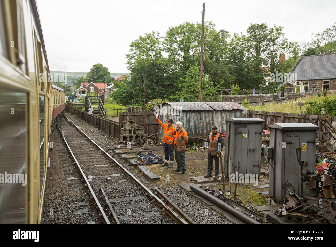 Eisenbahner neben Spuren tragen Warnkleidung winken für Passagiere mit Dampfzug nach Whitby England reisen Stockfoto