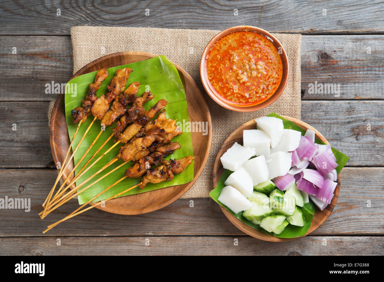 Draufsicht Malaysian Chicken Satay mit leckeren Erdnuss-Sauce, Ketupat, Zwiebeln und Gurken auf Holztisch, eines fa Stockfoto