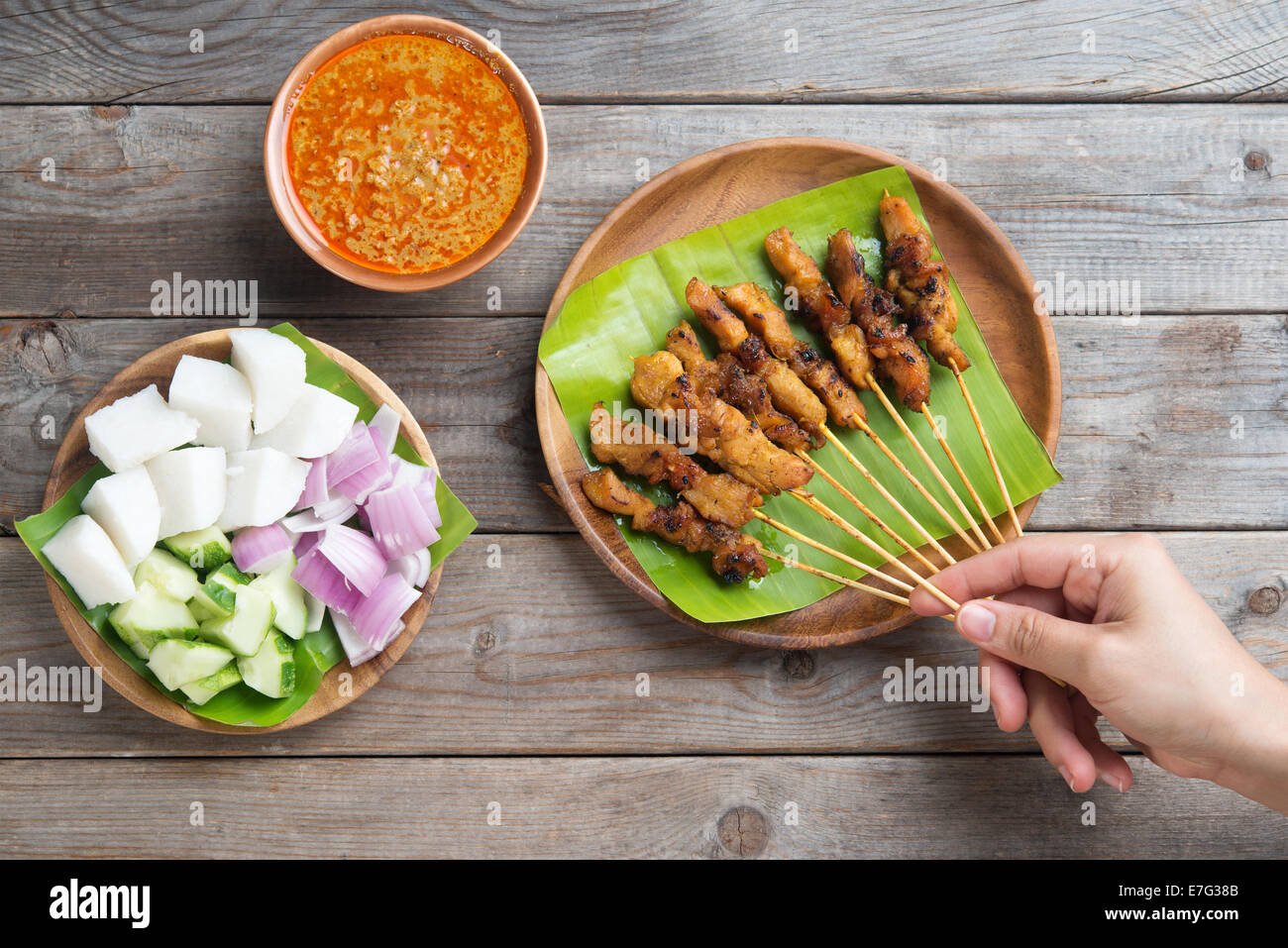 Draufsicht Leute halten Chicken Satay am Esstisch aus Holz, einer der berühmten lokalen Gerichten. Stockfoto
