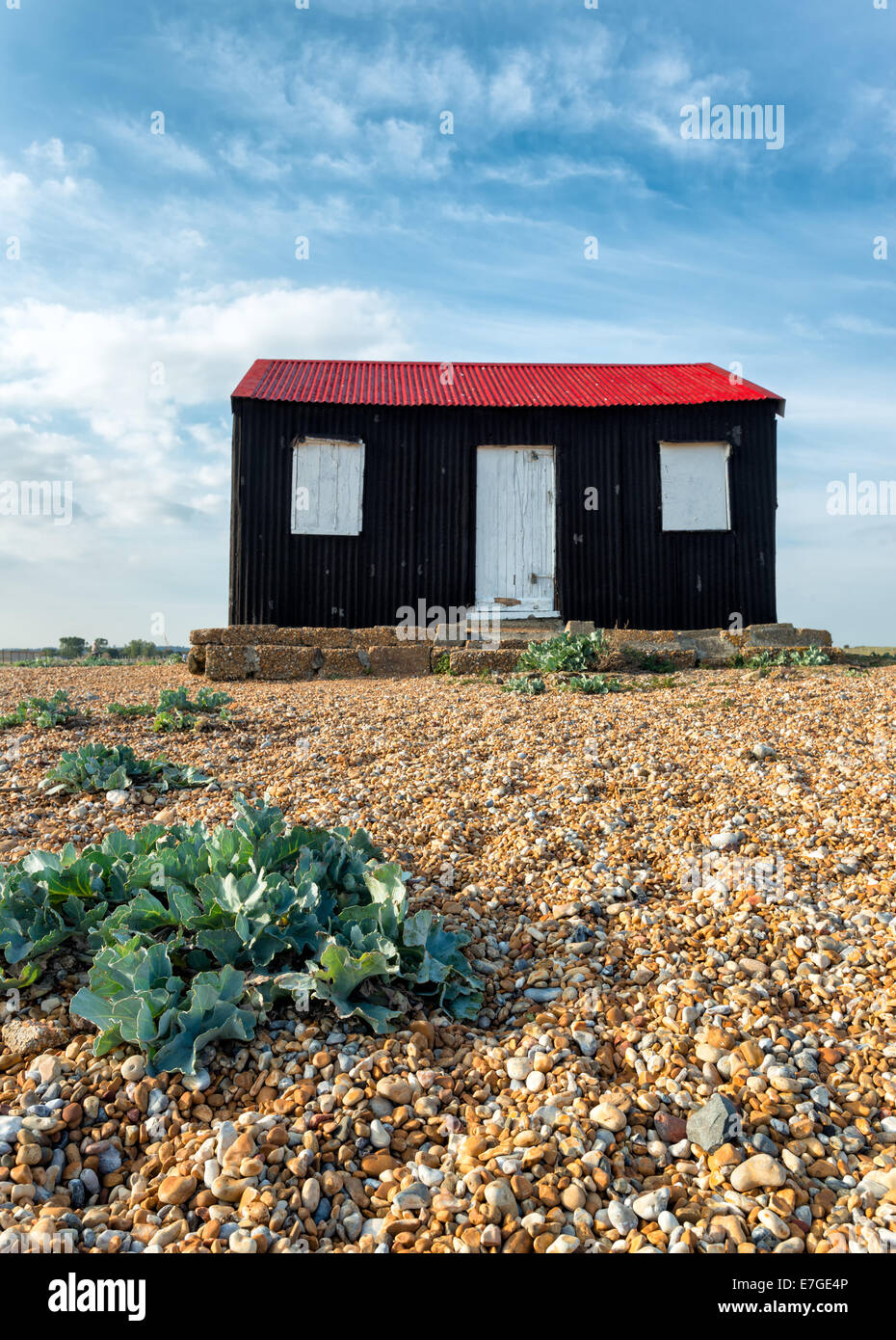 Eine schwarze Hütte mit einem roten Blechdach auf einem Kiesstrand bei Roggen in East Sussex Stockfoto