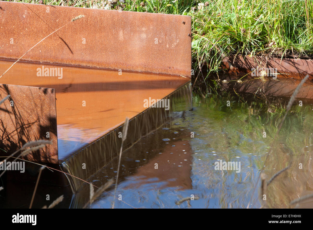 Wildtierfreundlicher Garten mit Rillenwasser aus rostem Kornstahl in einem kleinen Teich, in dem Ziergräser aus Großbritannien gepflanzt werden Stockfoto