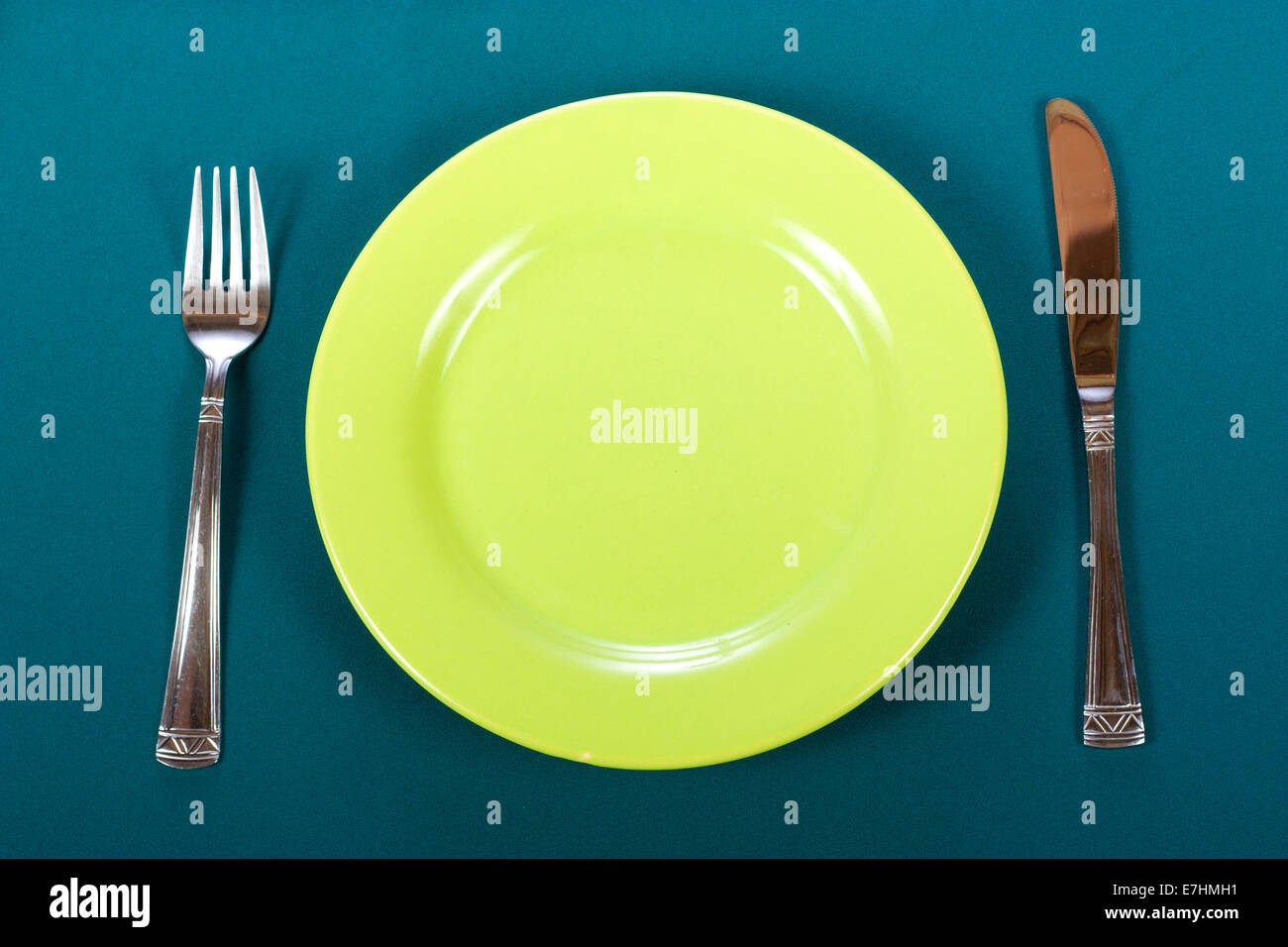 Messer, grüne Platte und Gabel auf Blaue Tischdecke Stockfoto