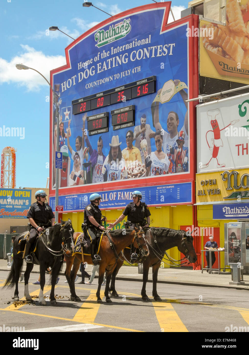 Helm tragen berittene Polizei auf Coney Island, New York City. Beachten Sie Werbeschild für das Hotdog-Wettessen in Nathans Restaurant, eine der Hauptattraktionen in diesem Vergnügungspark. Stockfoto