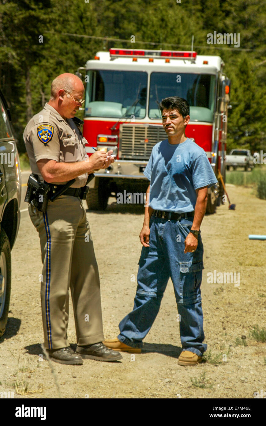 Nach einem Autounfall in Emerald Bay, CA interviews ein Polizist ein Hispanic Zeuge. Hinweis Feuerwehrauto im Hintergrund. Stockfoto