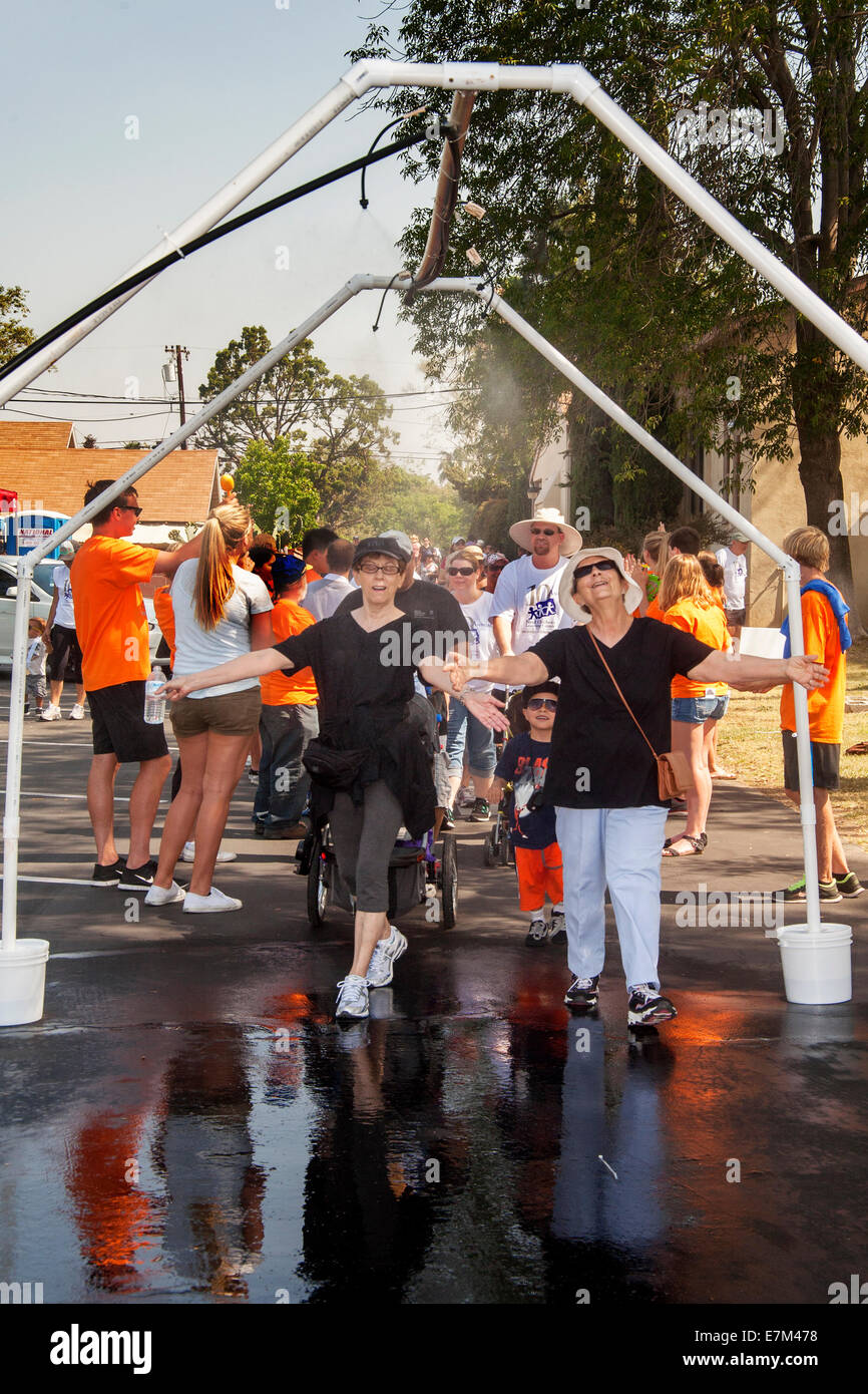 TeilnehmerInnen in eine Charity Fundraising Spaziergang an einem heißen Tag in Tustin, Kalifornien, erfrischen Sie sich unter einem Wasserstrahl an der Ziellinie. Stockfoto