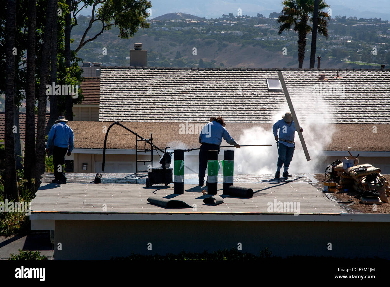 Dampf steigt aus heißem Teer als Hispanic Arbeiter ersetzen ein Garagendach in Laguna Niguel, CA. Hinweis Rollen Dachpappe. Stockfoto