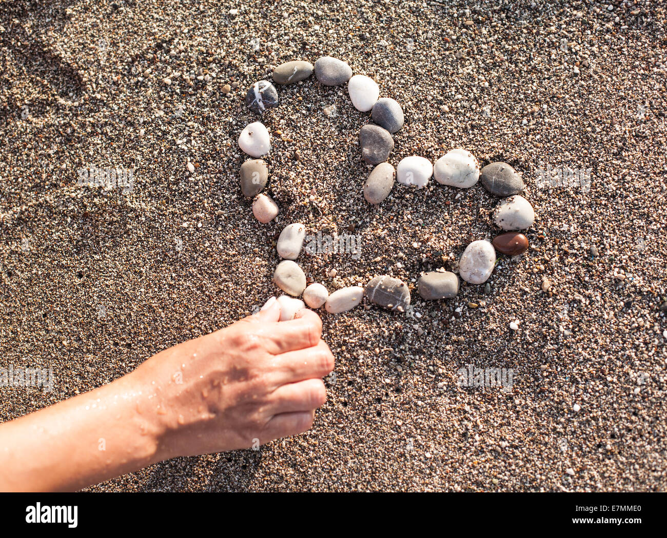 Zarte Frauenhand machen Herzen der marine Schindeln auf dem Sand. Stockfoto