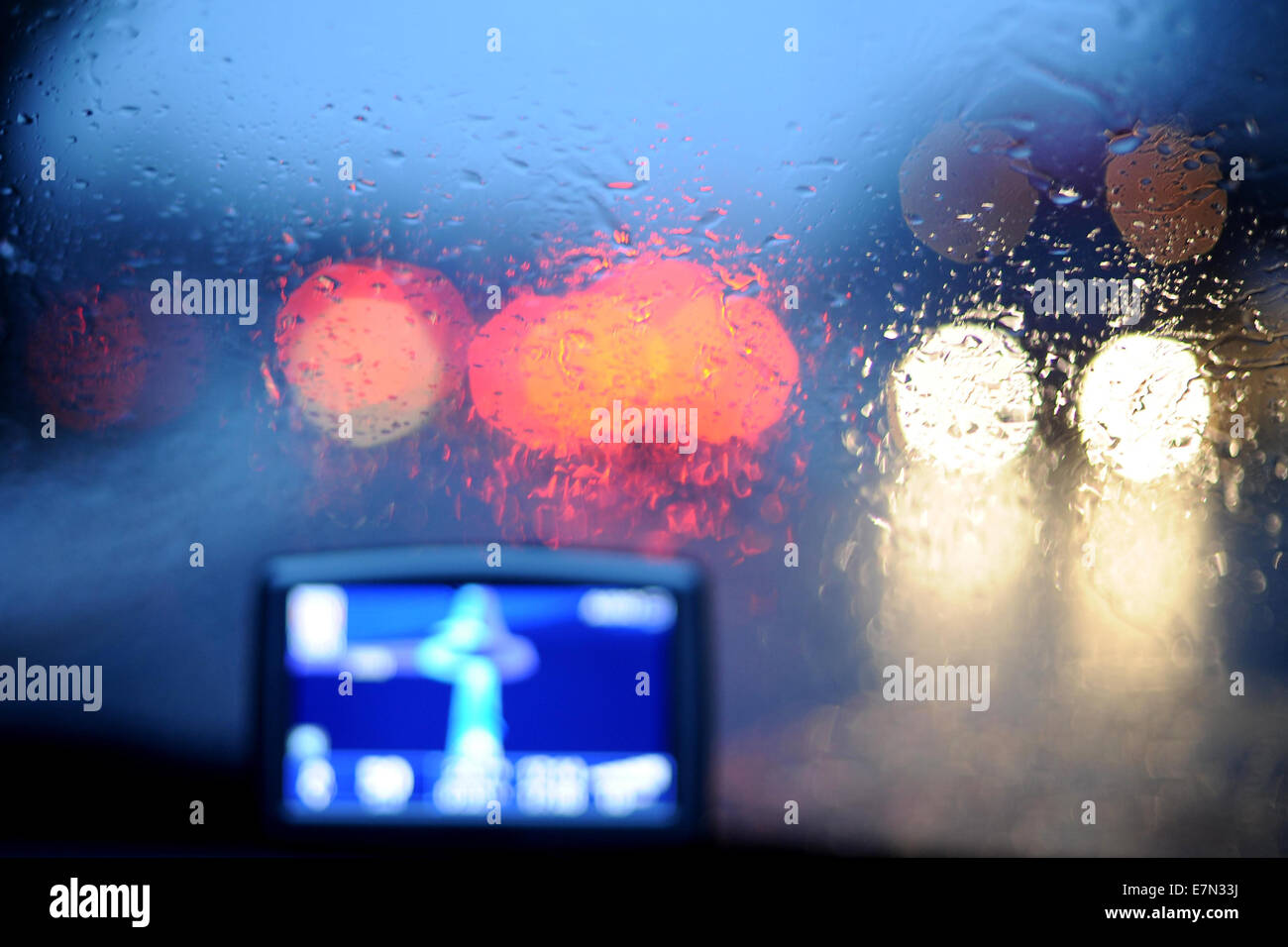Ein Navi im Auto bei Nässe und Regen mit Bremslicht und Autoscheinwerfer durchscheinen der Windschutzscheibe verwendet wird. Stockfoto