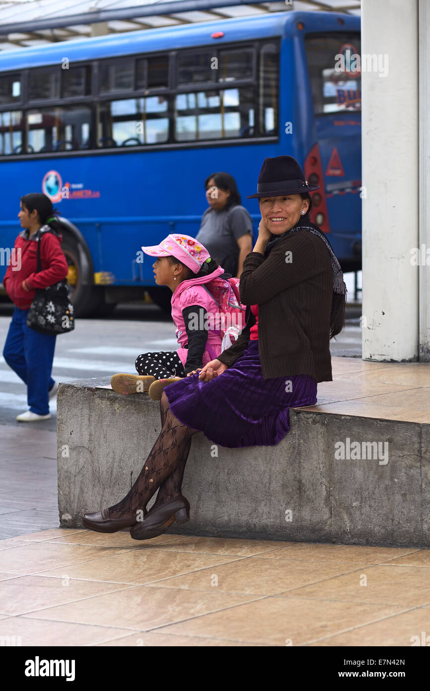 Unbekannte Frau und Mädchen sitzen auf einer Plattform des Ortsbusses station außen Terminal Terrestre Quitumbe in Quito, Ecuador Stockfoto