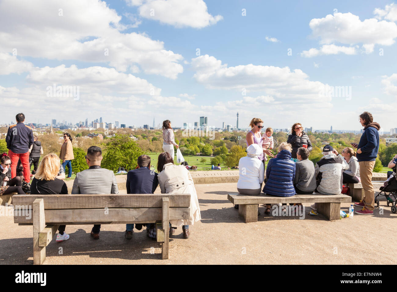 London Aussichtspunkt. Leute sitzen auf Bänken in der Frühlingssonne die entfernte Skyline der Stadt von Primrose Hill, London, England, Großbritannien Stockfoto